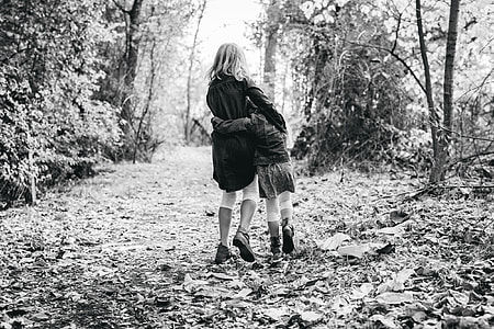 two girls walking on leaf-covered road in forest thumbnail