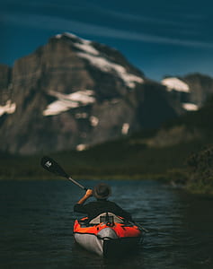 man in black dress shirt and hat on red inflatable raft paddling near mountain on blue ocean water during daytime thumbnail