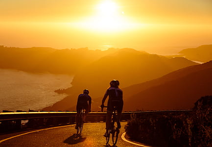 two people riding bicycles on bridge near body of water during sunset thumbnail