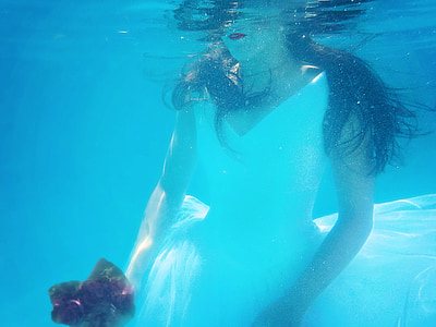 woman wearing white v-neck sleeveless dress holding red flower bouquet under water thumbnail