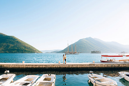man front of woman on wooden dock near motorboats during daytime thumbnail