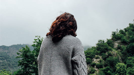 woman in grey knit top standing facing green mountain thumbnail