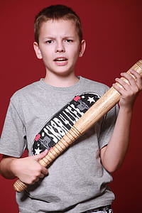 boy holding baseball bat standing near red wall thumbnail