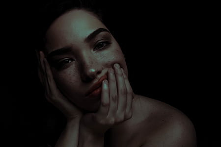 woman holding her face while looking straight to the camera on dark surface thumbnail
