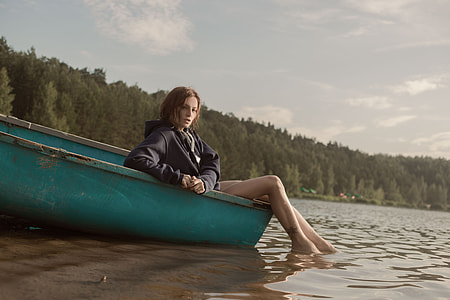 woman in black jacket sitting on green boat near trees during daytime thumbnail