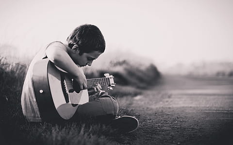 boy playing a guitar while sitting on grass field thumbnail