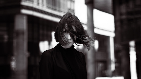 gray scale photo of woman wearing turtle-neck shirt on building background thumbnail