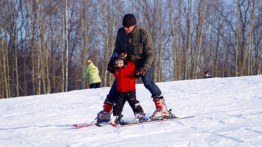 man and child standing on snow ski on snow field near bare trees at daytime thumbnail