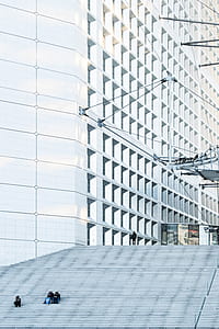 three person's sitting on stairs near white concrete structure thumbnail