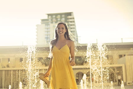 Beautiful Young Woman In Yellow Spaghetti Strap Dress Stands Near Water Fountain thumbnail