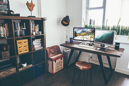 photo of two flat screen computer monitors on brown wooden table beside cube shelf inside room thumbnail