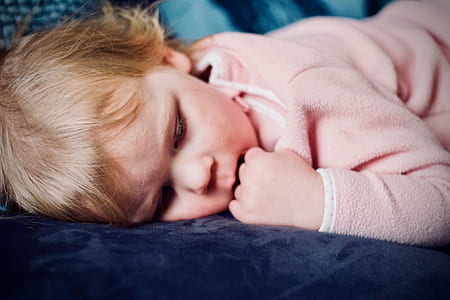 baby putting hands on mouth lying on blue bedspread thumbnail