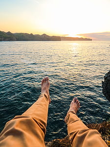 Person Wearing Yellow Pants Sitting on Rock Surrounded by Sea thumbnail