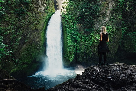woman wearing black sleeveless dress standing in front of waterfalls thumbnail