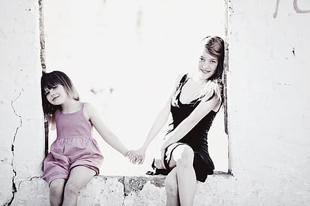 woman in black sleeveless dress and girl in pink spaghetti strap top sitting in gray floor thumbnail