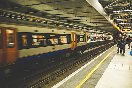 man and woman standing near white, orange, and blue train thumbnail