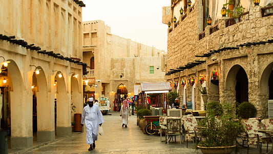 man in white thawb robe walking in front of concrete building thumbnail