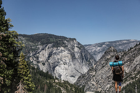 man standing on cliff facing mountain landscape during daytime thumbnail
