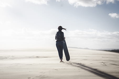 woman walking while holding surfboard during daytime thumbnail