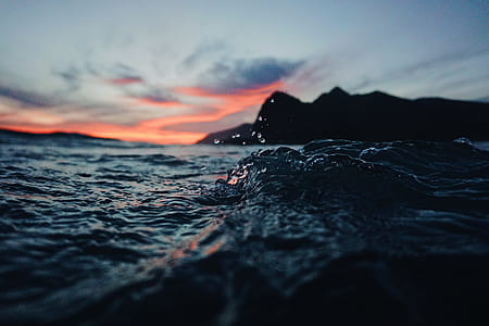 photo of black mountain against orange skies taken above body of water thumbnail