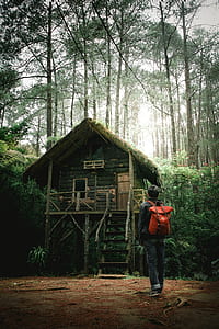man standing while carrying backpack near brown house at daytime thumbnail