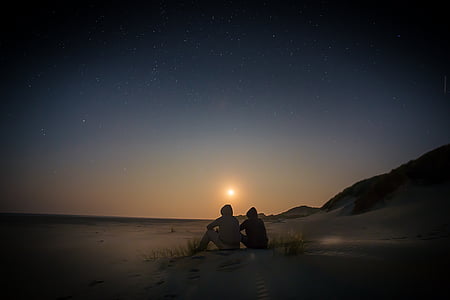 two person sitting on seashore near sea during golden hour thumbnail
