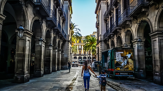 woman and boy walking between brown buildings during daytime thumbnail