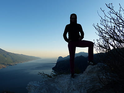 silhouette of person standing on hill viewing body of water and mountain range thumbnail
