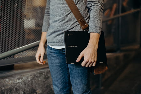person carrying black Samsung Chromebook near brown steel fence thumbnail