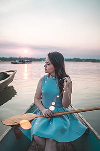 woman sitting on blue boat while holding brown wooden paddle on lap thumbnail