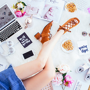 woman sitting on rug surrounded with laptop, flowers, art materials, and shoes flatlay photography thumbnail