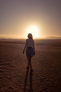 woman standing on brown sand during sunset thumbnail