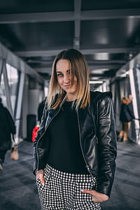 woman in black leather jacket standing inside gray building thumbnail