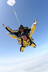 man and woman wearing yellow suit riding parachute above clouds thumbnail