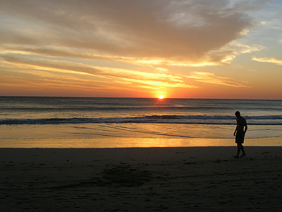 silhouette dusk photo of man walking on sea shore during golden time thumbnail