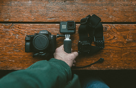 person holding black GoPro HERO beside black Canon camera thumbnail