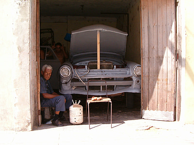man sitting on stool near white gas tank and classic blue car body shell in garage during daytime thumbnail