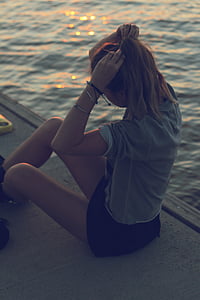 woman in gray shirt sitting on pier fixing her hair thumbnail