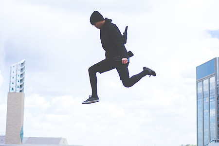 photography of man wearing black beanie, black top, black pants, and black low top sneakers jumping under gray sky thumbnail