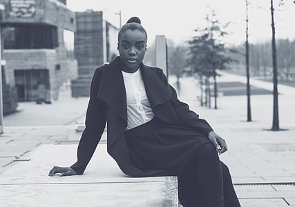 grayscale photo of woman sitting on concrete bench thumbnail