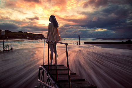 woman standing on brown wooden platform wearing pink long-sleeved blouse low exposure photography thumbnail