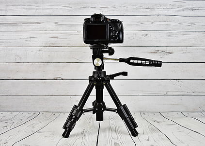 black camera with black tripod stand on white wooden surface thumbnail