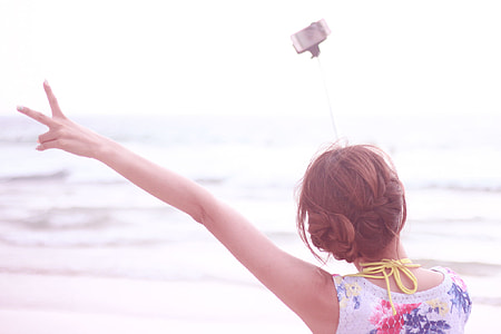 woman wearing white and red floral top wear using monogram to have selfie beside seashore during daytime thumbnail