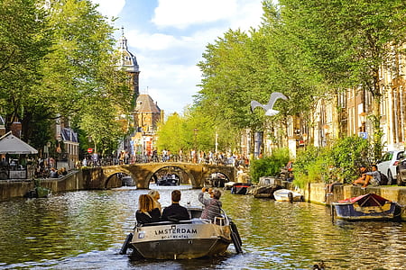 people on motorboat between buildings moving towards the footed bridge under white sky at daytime thumbnail