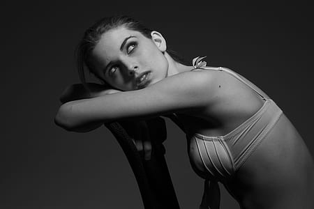 woman wearing brassier leaning on chair backrest in greyscale photography thumbnail