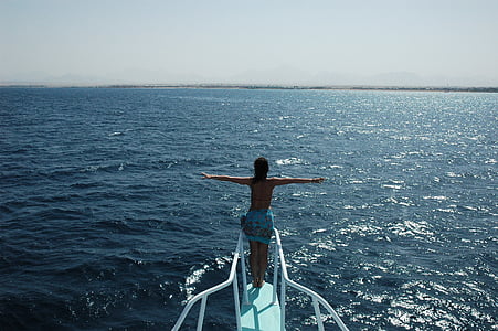woman standing on ship's edge facing blue ocean thumbnail