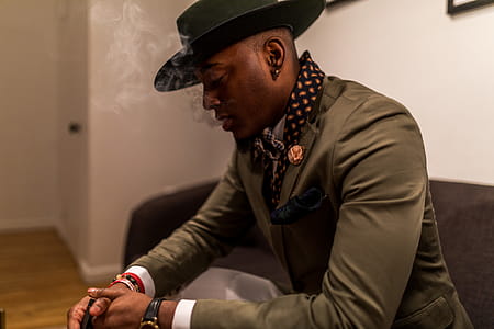 Man in Green Blazer With Cap Sitting on Black Sofa thumbnail