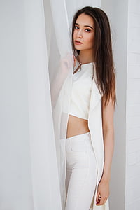 woman wearing white split-neck crop top holding white curtain inside white painted room thumbnail
