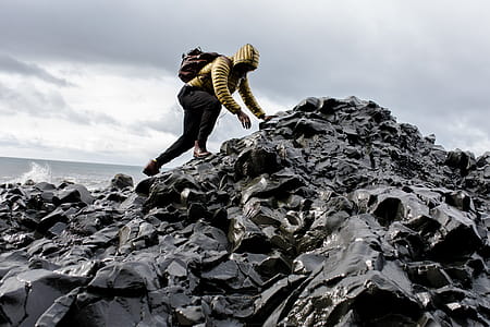 Man Wearing Hoodie and Black Pants Climbing Up Pile of Rocks thumbnail