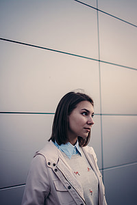 woman in beige jacket standing near wall thumbnail
